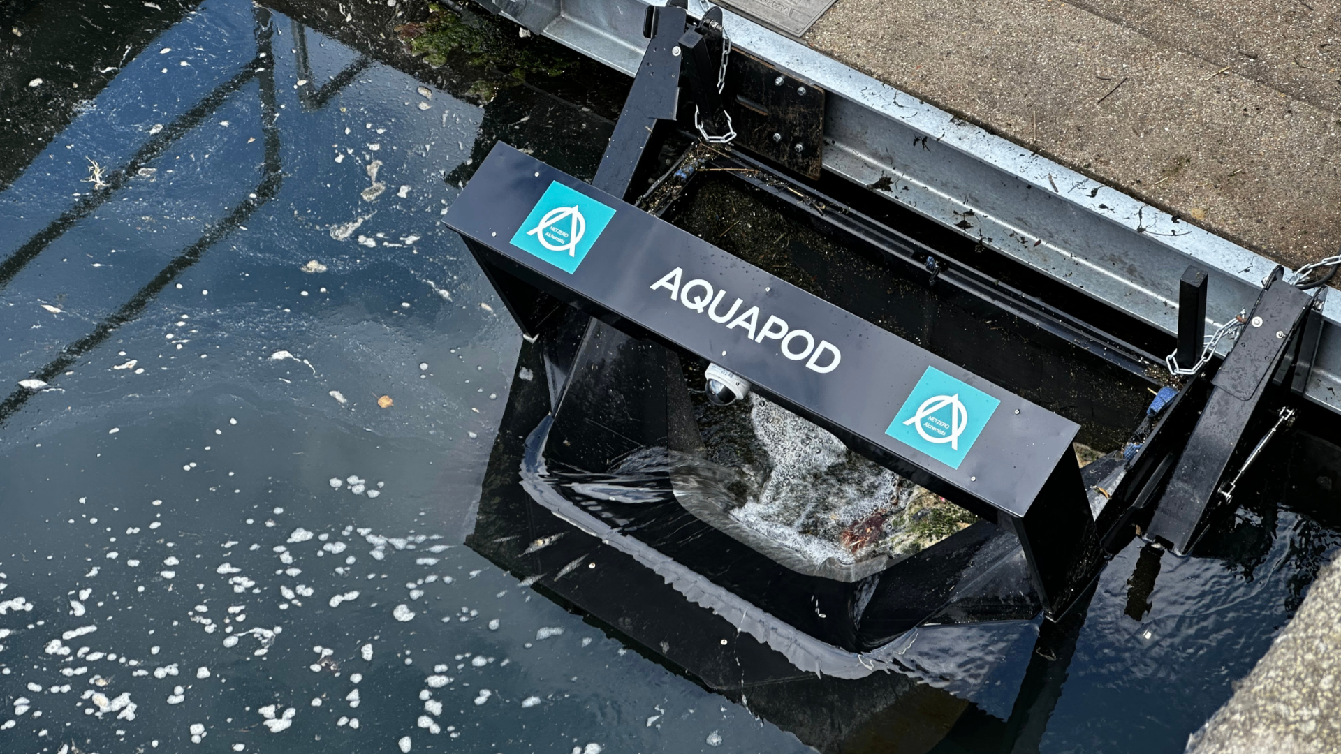 Top-down view of a branded NETZERO Alchemists Aquapod collecting floating debris at Belfast Harbour